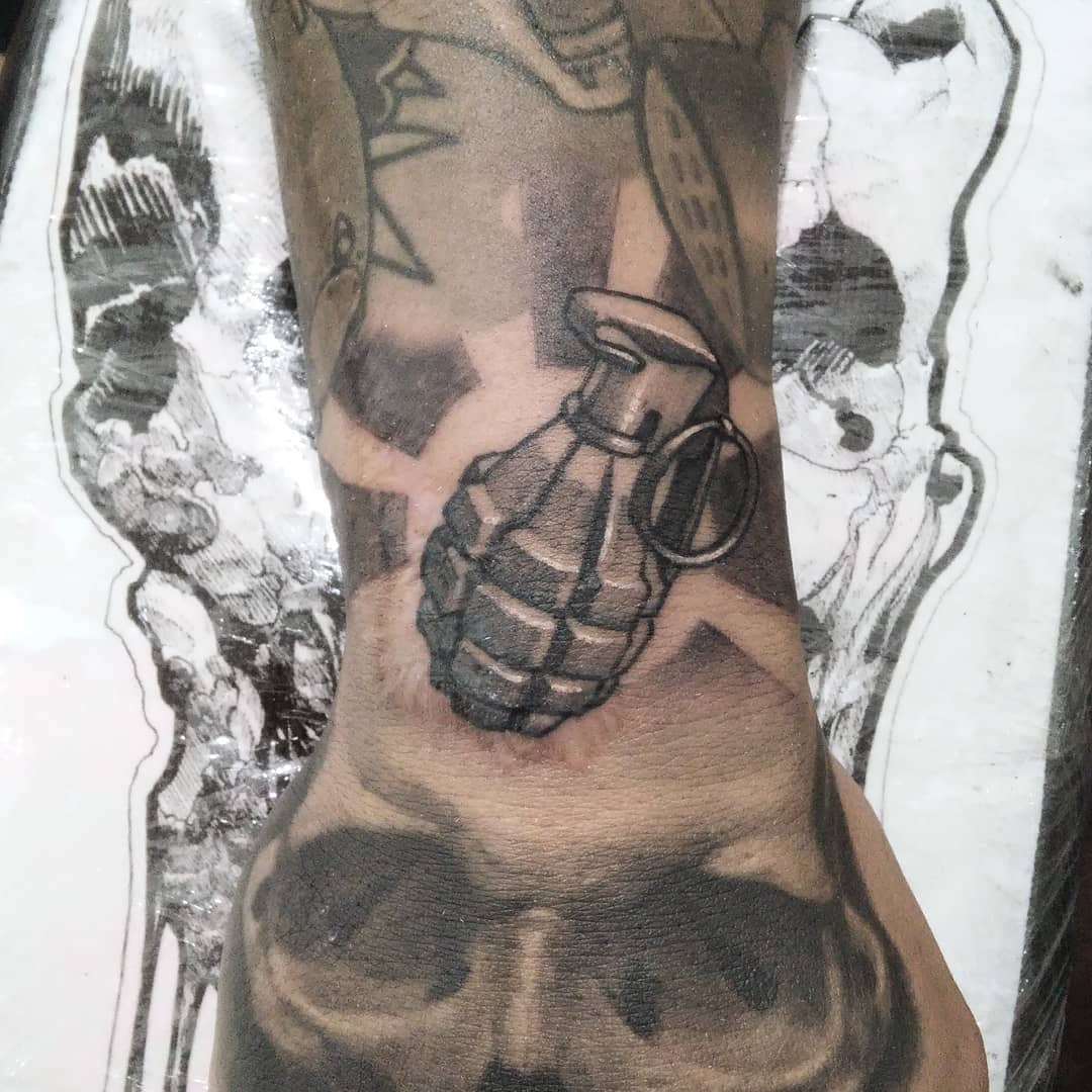 Tatuaje blackwork de granada y calavera en el dorso de la mano