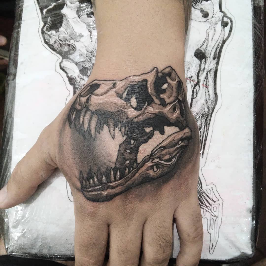 Tatuaje ilustrativo de cráneo de dinosaurio en el dorso de la mano